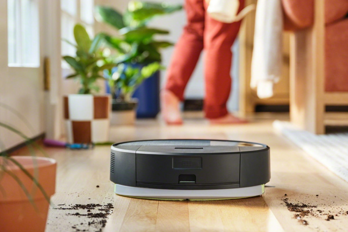 Roomba odkurza piach, w tle kobieta zajmuje się kwiatami
