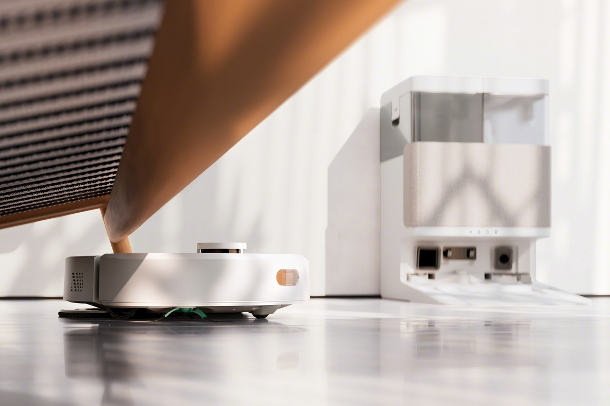 Robot Roomba Plus 405 Combo sprząta pod kanapą w salonie, w tle widać stację AutoWash