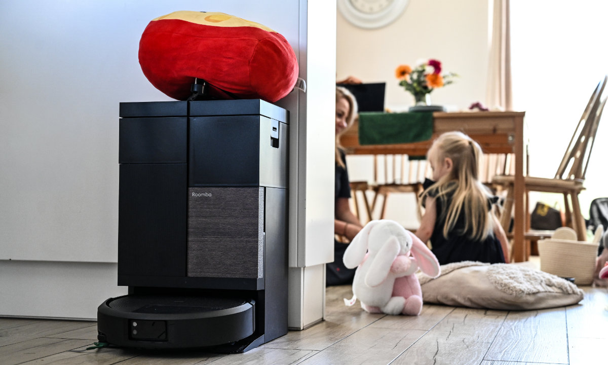 Robot Roomba stoi w stacji AutoWash, na drugim planie widać mamę bawiącą się z córką