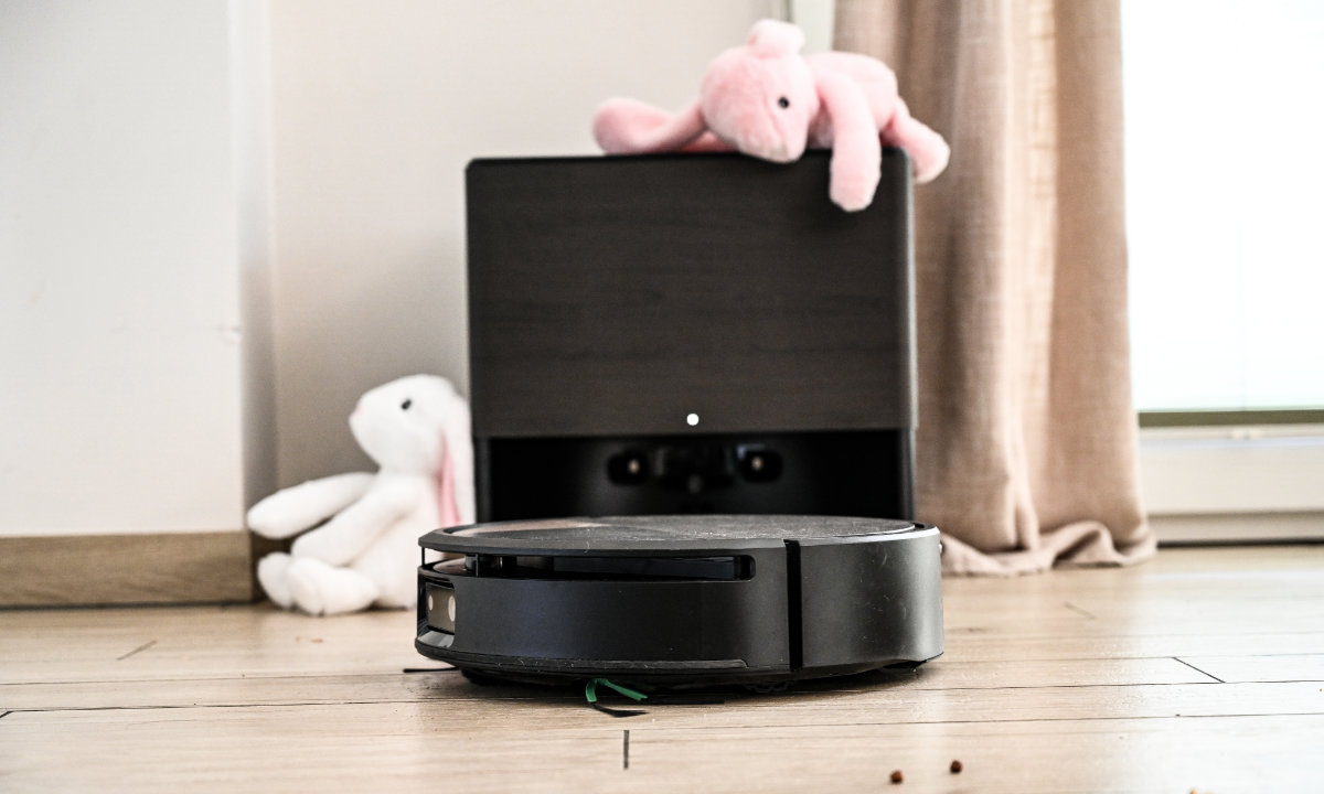 Robot Roomba stoi w stacji AutoWash, dookoła leżą pluszowe króliki