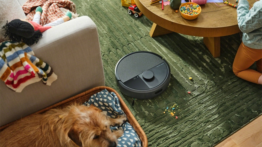 Pies leży na legowisku podczas gdy robot sprzątający odkurza pdłogę w salonie