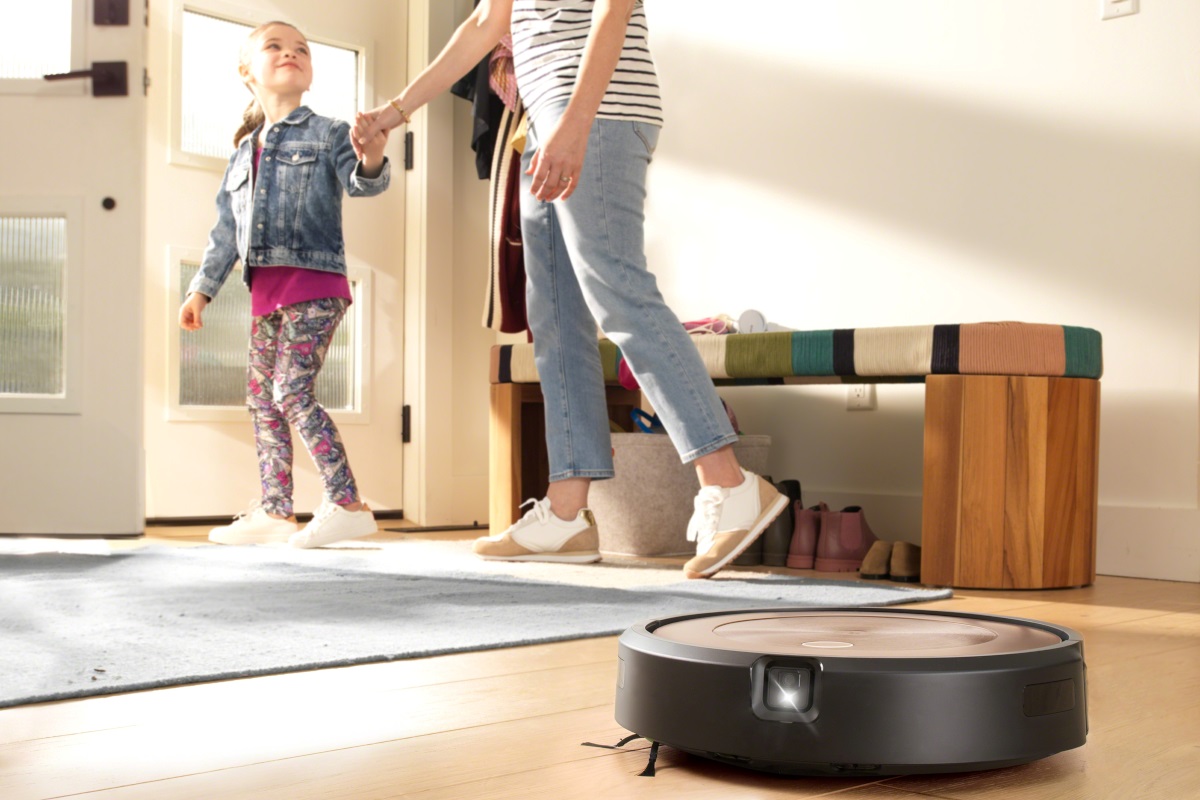 Mama z córką wychodzą z domu, trzymając się za ręce, a w tym czasie Roomba sprząta podłogę.