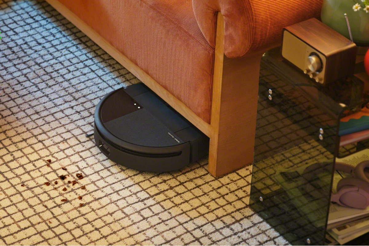 iRobot Roomba 205 wyjeżdza spod kanapy w kierunku zabrudzenia na podłodze