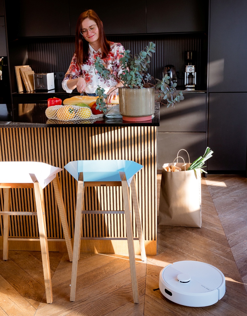 Robot Roomba 105 Combo sprząta w kuchni podczas gdy kobieta przygotowuje posiłek