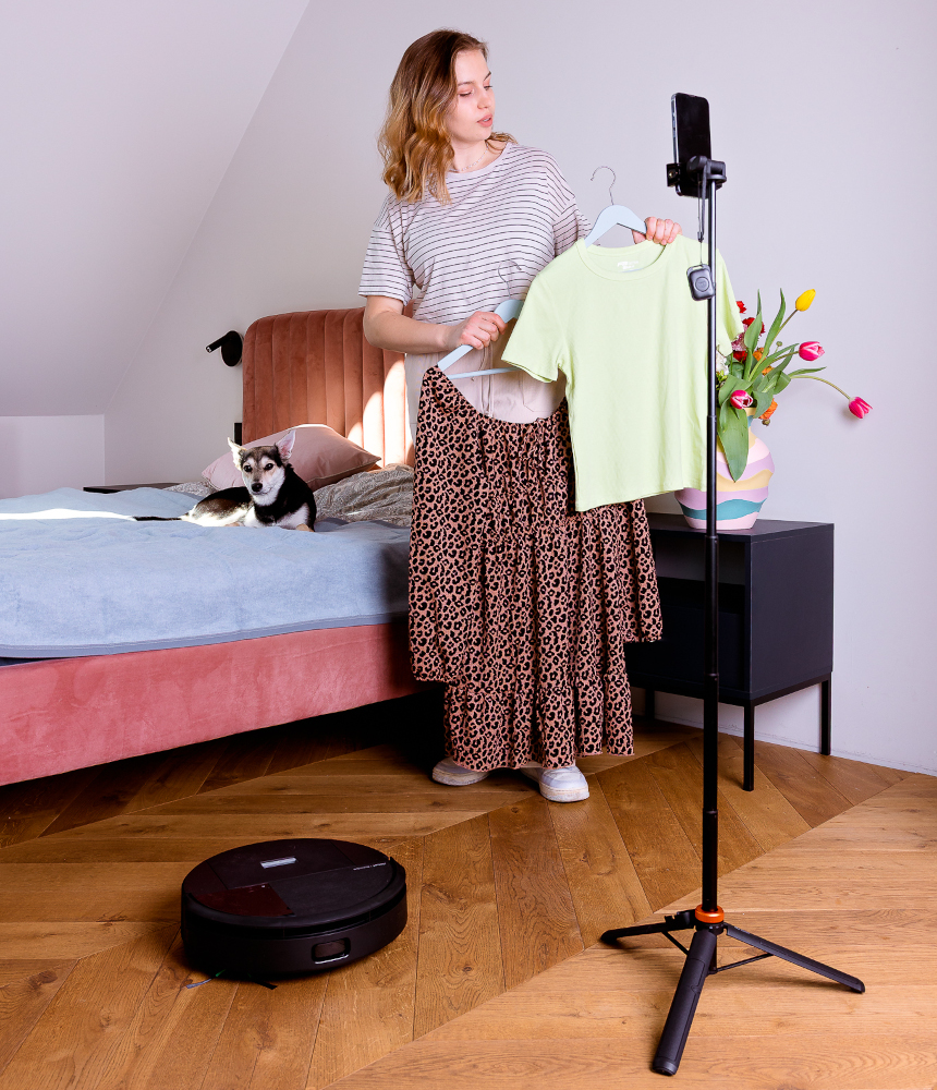 Kobieta trzyma wieszaki z ubraniami, w tle na łóżku leży pies