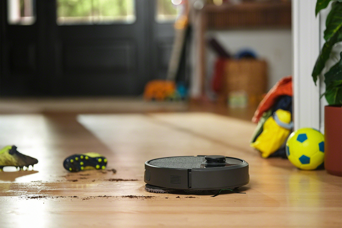 Roomba 405 podczas mopowania podłogi. Obok buty do gry w piłkę nożną