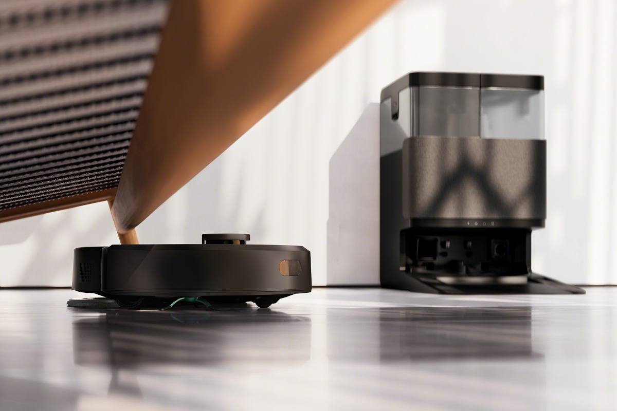 iRobot Roomba 405 wyjeżdża spod kanapy, w tle stacja AutoWash