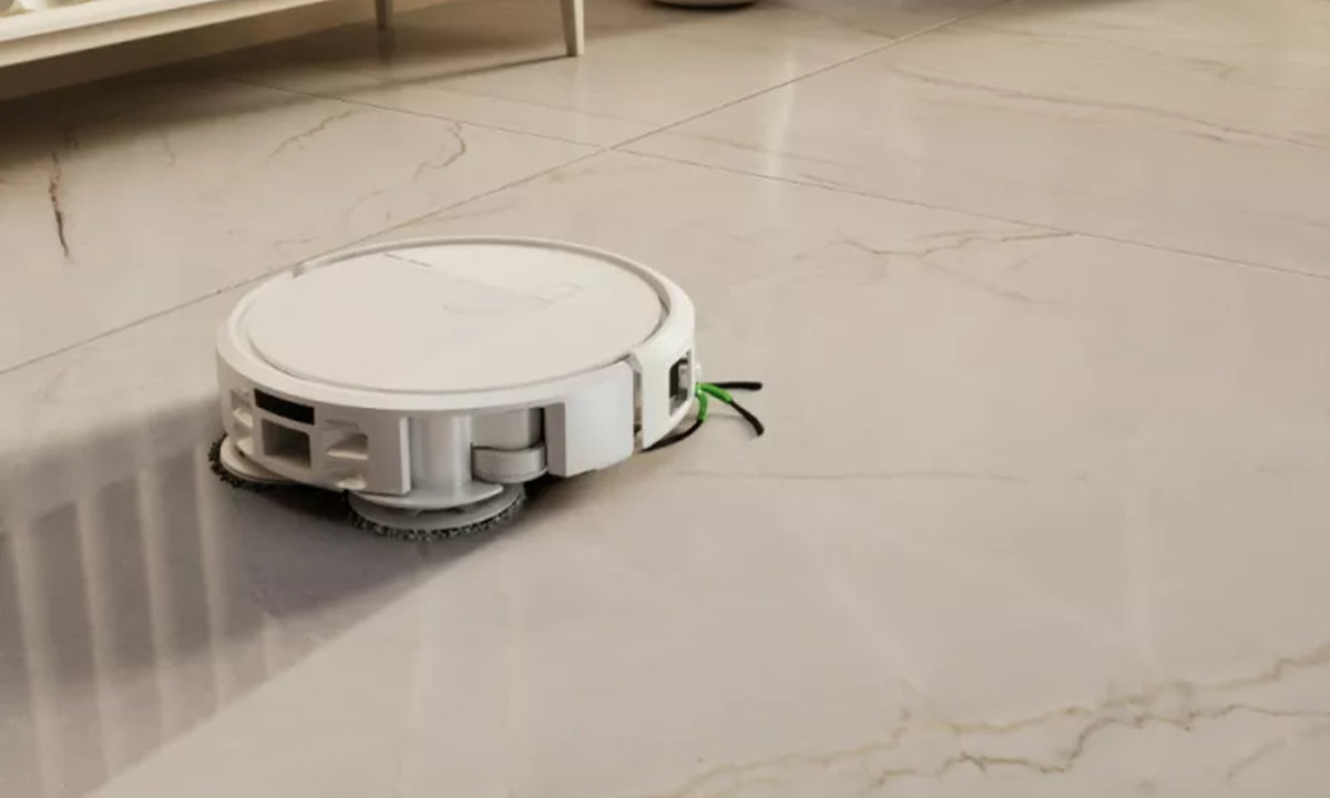 Roomba Plus 575 sprząta twardą podłogę w salonie kierując się w stronę nowoczesnej komody i jasnej sofy
