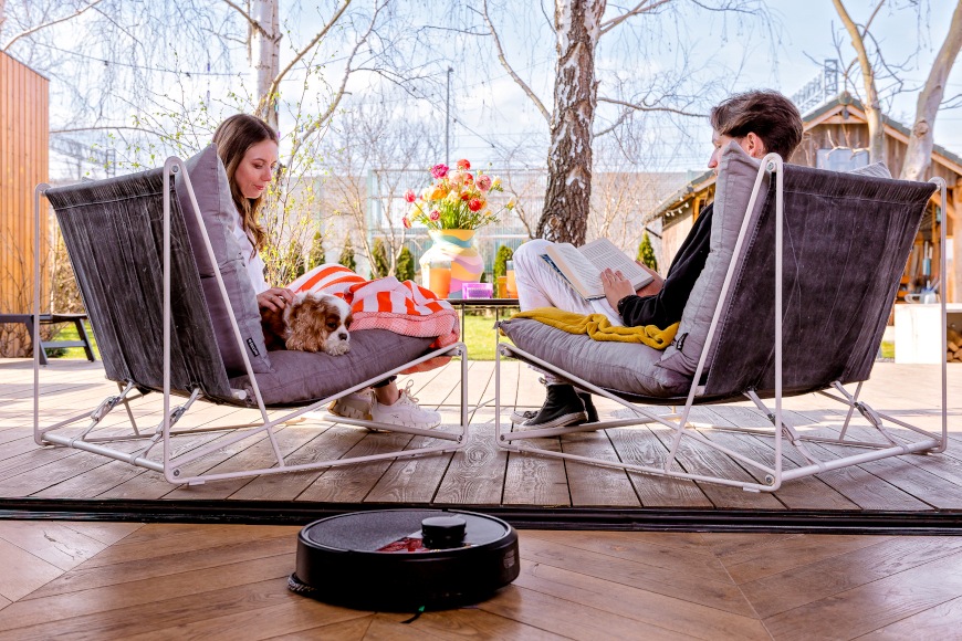 Małżeństwo z psem siedzi na tarasie wychodzącym na ogród, na pierwszym planie Roomba Plus 405 Combo odkurza panele
