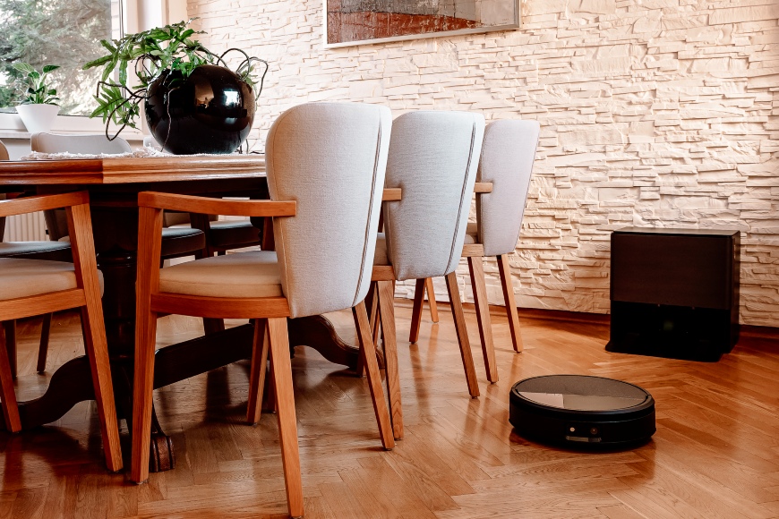 Roomba Max 705 Combo odkurza i mopuje wokół stołu w jadalni, pod ścianą widoczna stacja dokująca AutoWash