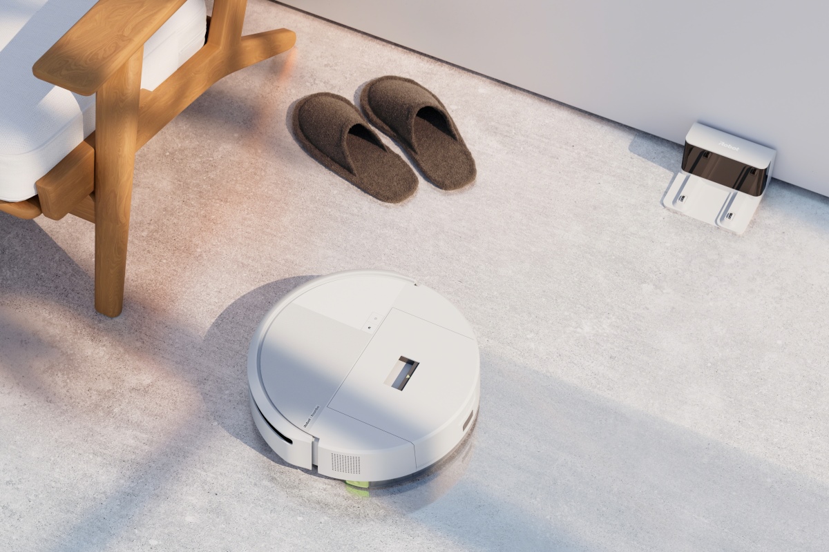 Roomba 205 odkurza dywan, obok leżą kapcie