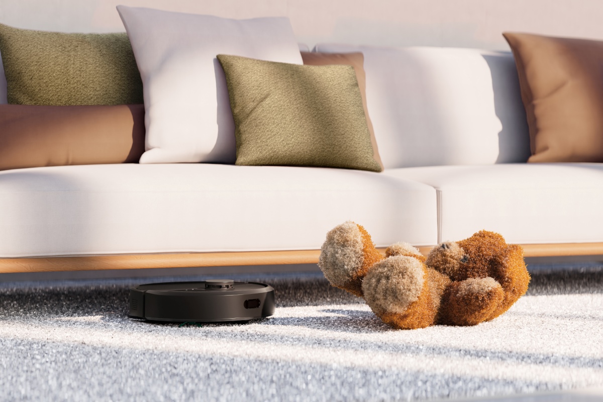 Roomba 405 sprząta dywan pod kanapą, na podłodze leży maskotka