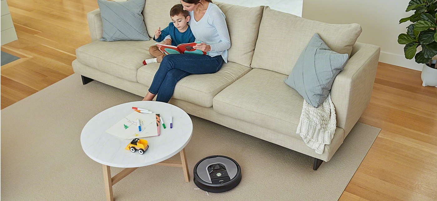 iRobot Roomba serii 900 odkurza pokój a na kanapie siedzi mama z dzieckiem