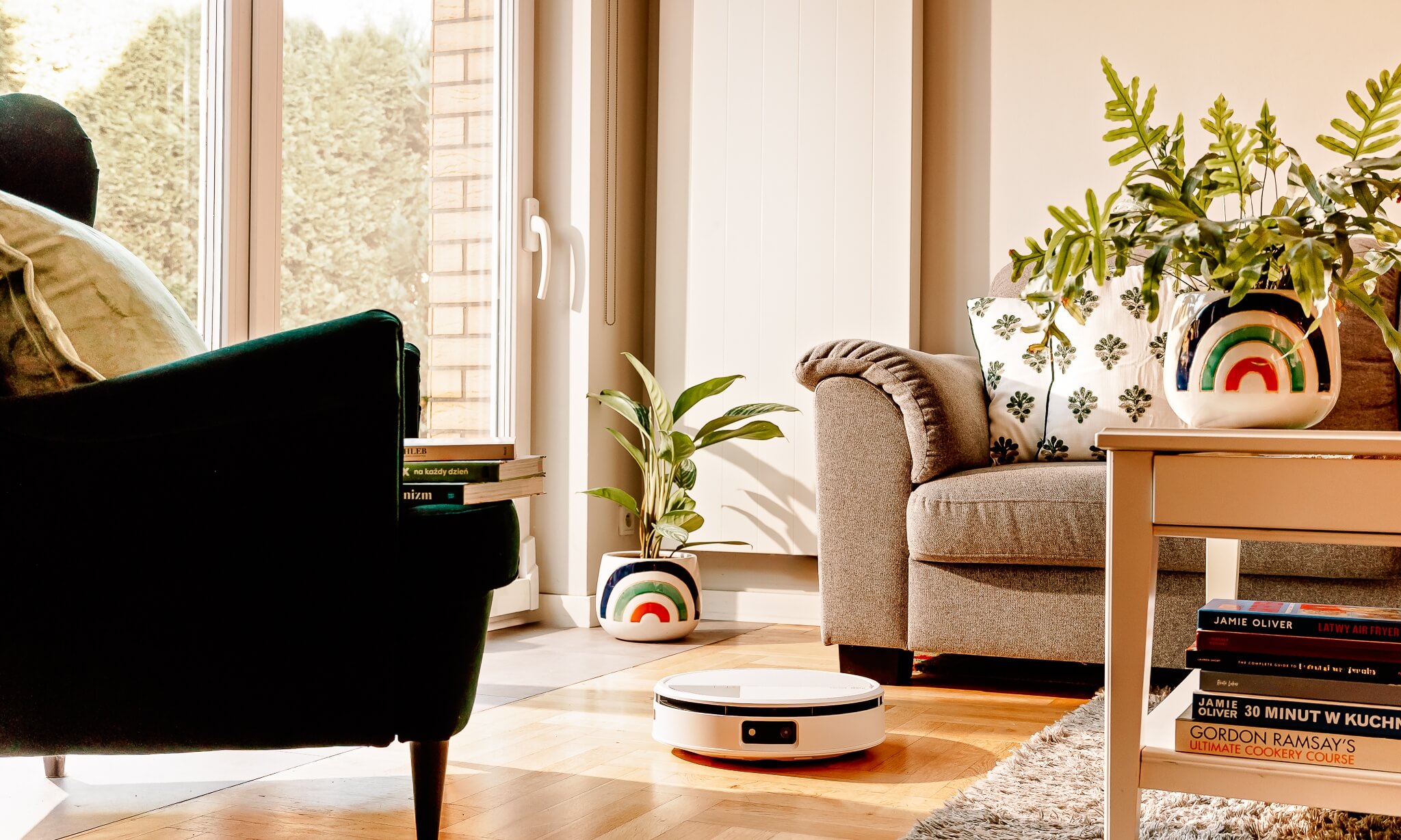 Robot Roomba Max 705 Combo sprząta w salonie pomiędzy szarą sofą, zielonym fotelem a stolikiem kawowym