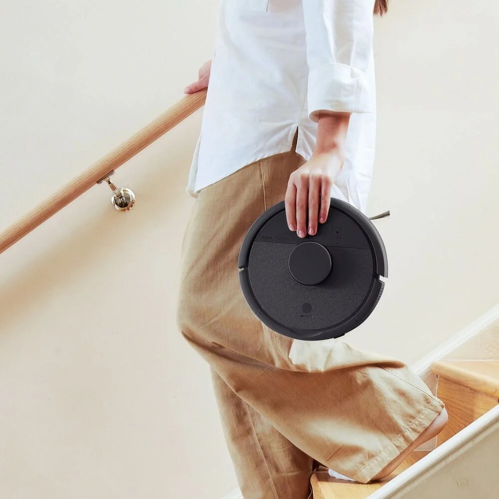 Kobieta schodzi po schodach i niesie w ręku robota Roomba Mini Combo