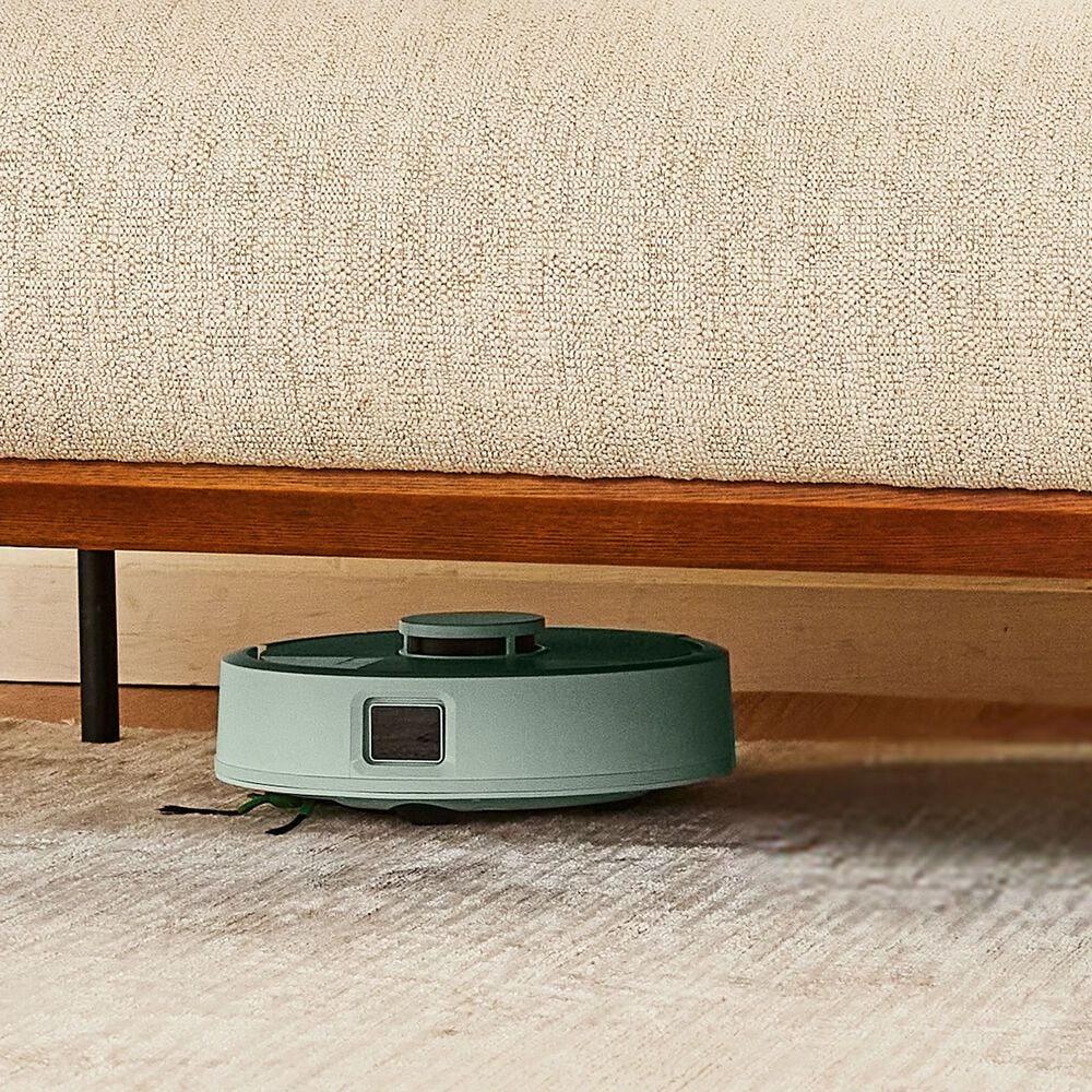 Roomba Mini sprząta pod niską sofą na dywanie w salonie