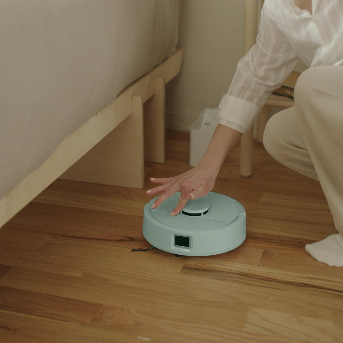Kobieta naciska na przycisk sprzątania na robocie Roomba Mini Combo, uruchamiając sprzątanie w sypialni