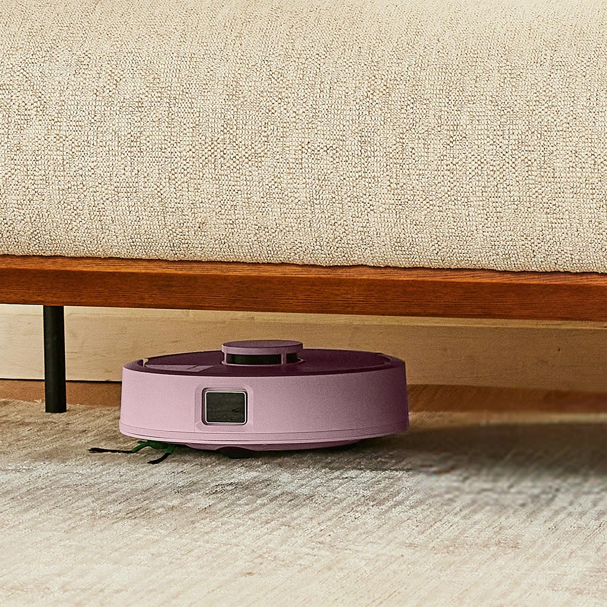 Roomba Mini sprząta pod niską sofą na dywanie w salonie