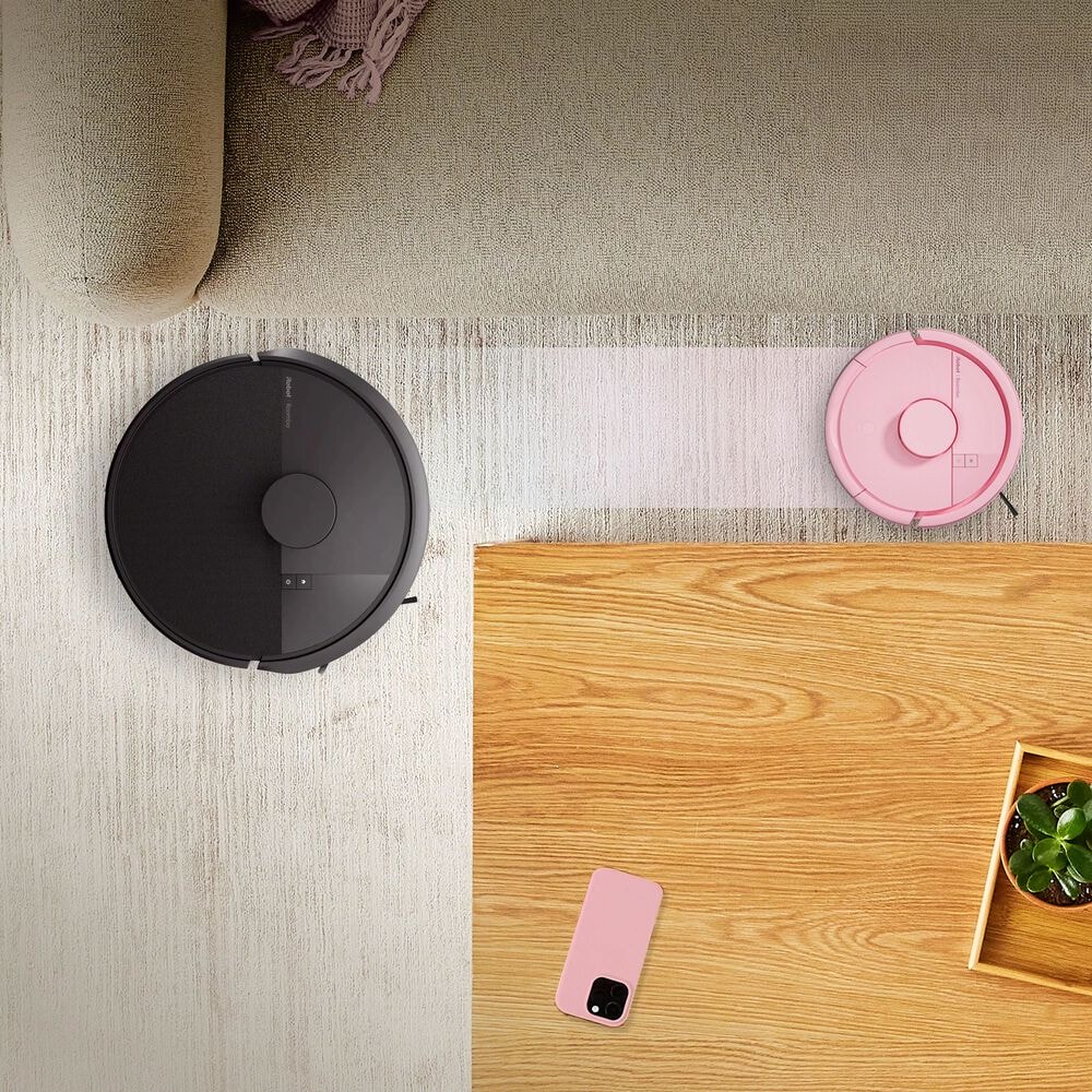 Robot Roomba Mini przejeżdża wąską ścieżką między kanapą a stolikiem kawowym, obok Roomba 105 Combo