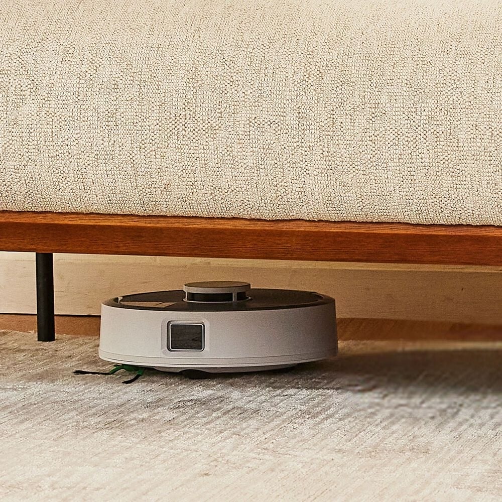 Roomba Mini sprząta pod niską sofą na dywanie w salonie