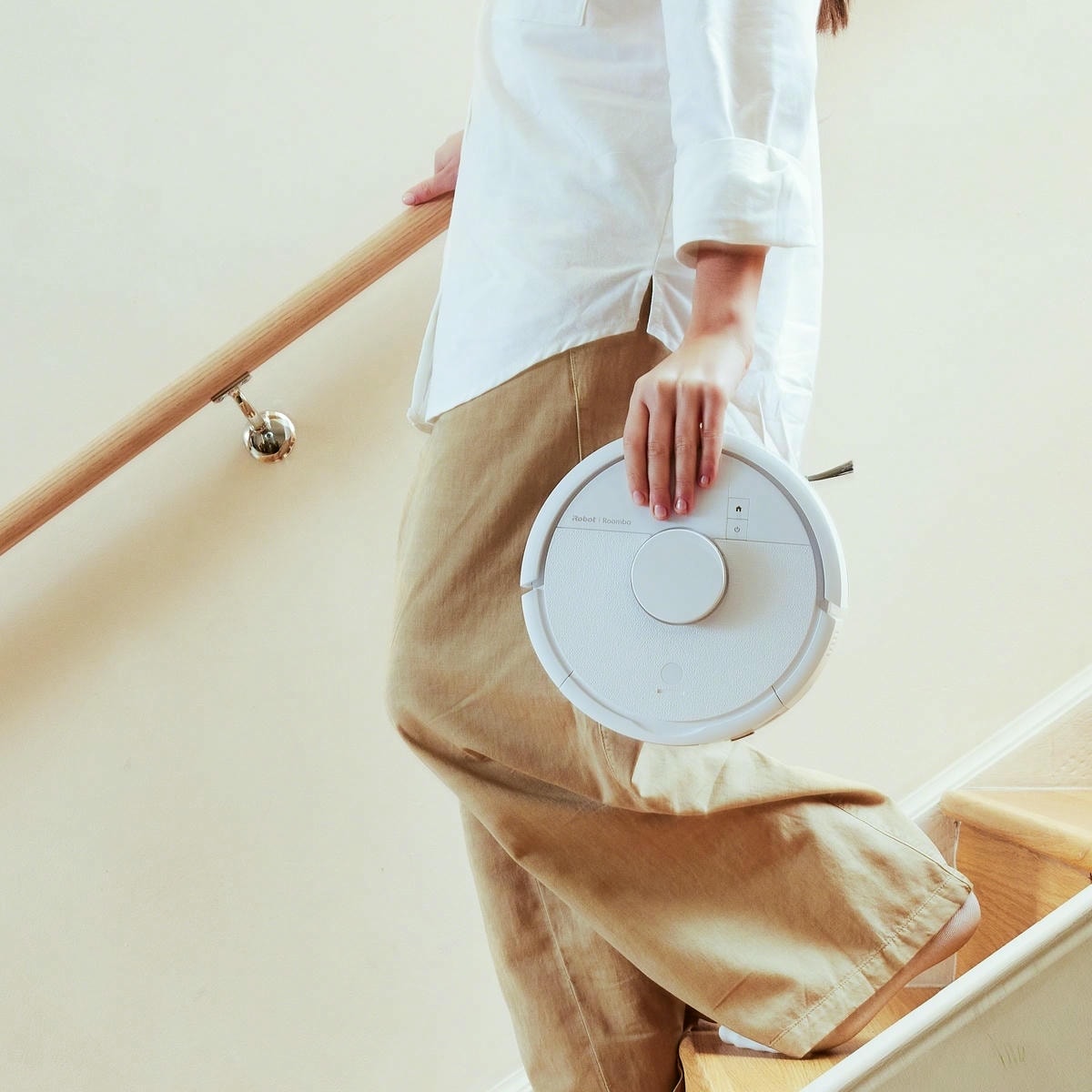 Kobieta schodzi po schodach i niesie w ręku robota Roomba Mini Combo