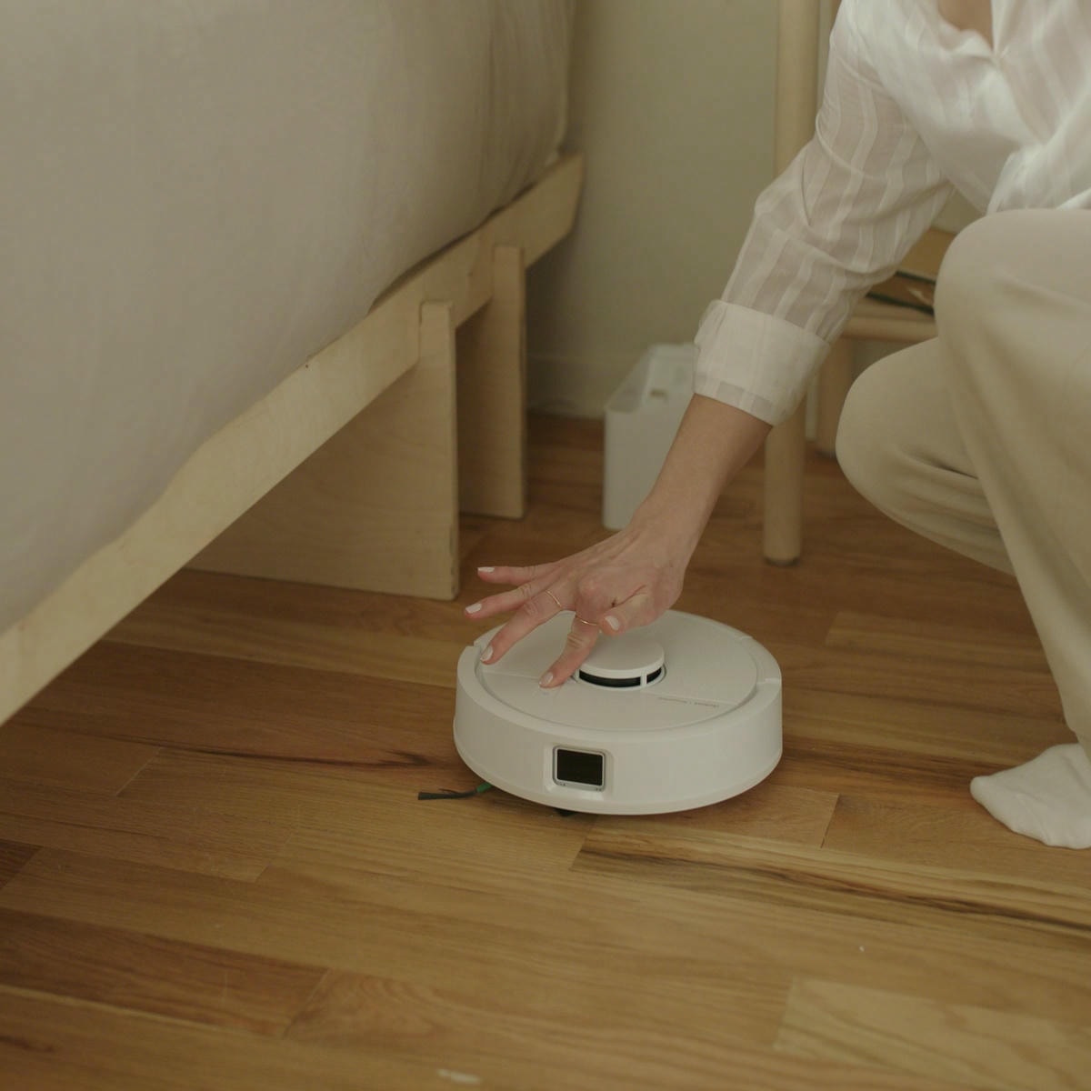 Kobieta naciska na przycisk sprzątania na robocie Roomba Mini Combo, uruchamiając sprzątanie w sypialni