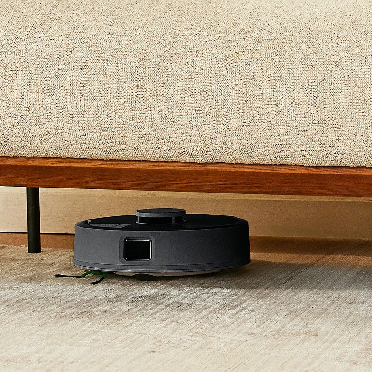 Roomba Mini sprząta pod niską sofą na dywanie w salonie